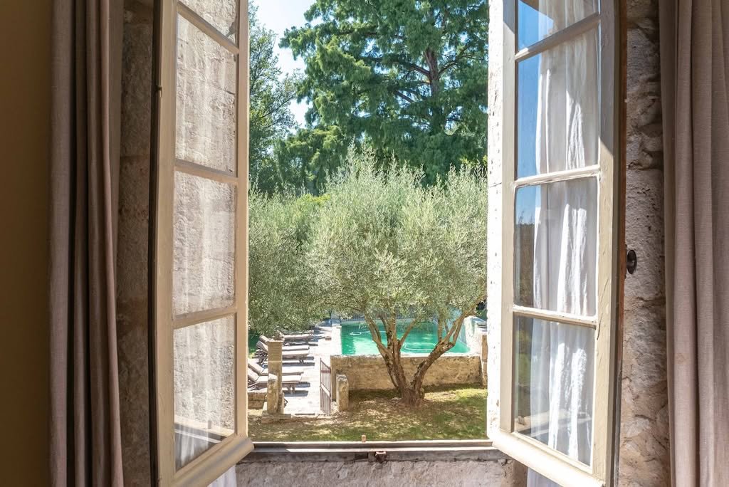 A window looking out over the pool and olive trees