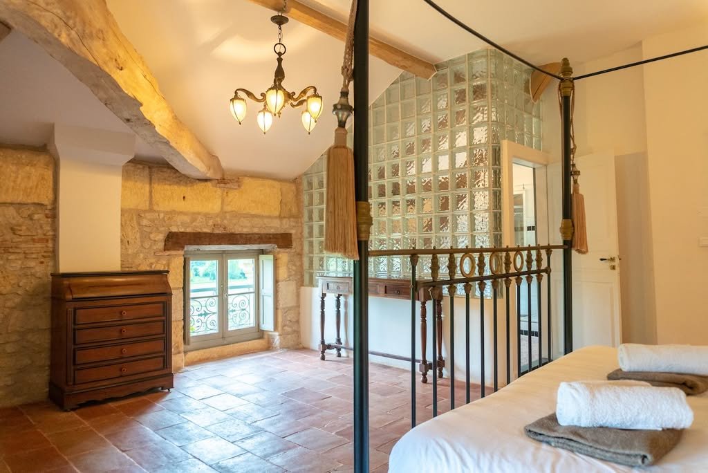 A four-poster bedroom with stone walls and a glass-brick bathroom